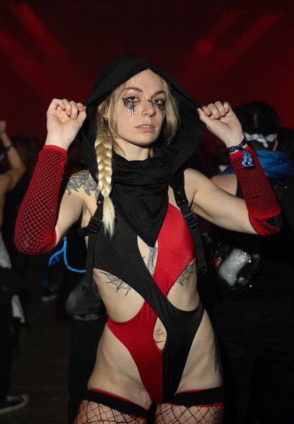 Person in a red and black costume with tattoos, standing against a dark background.